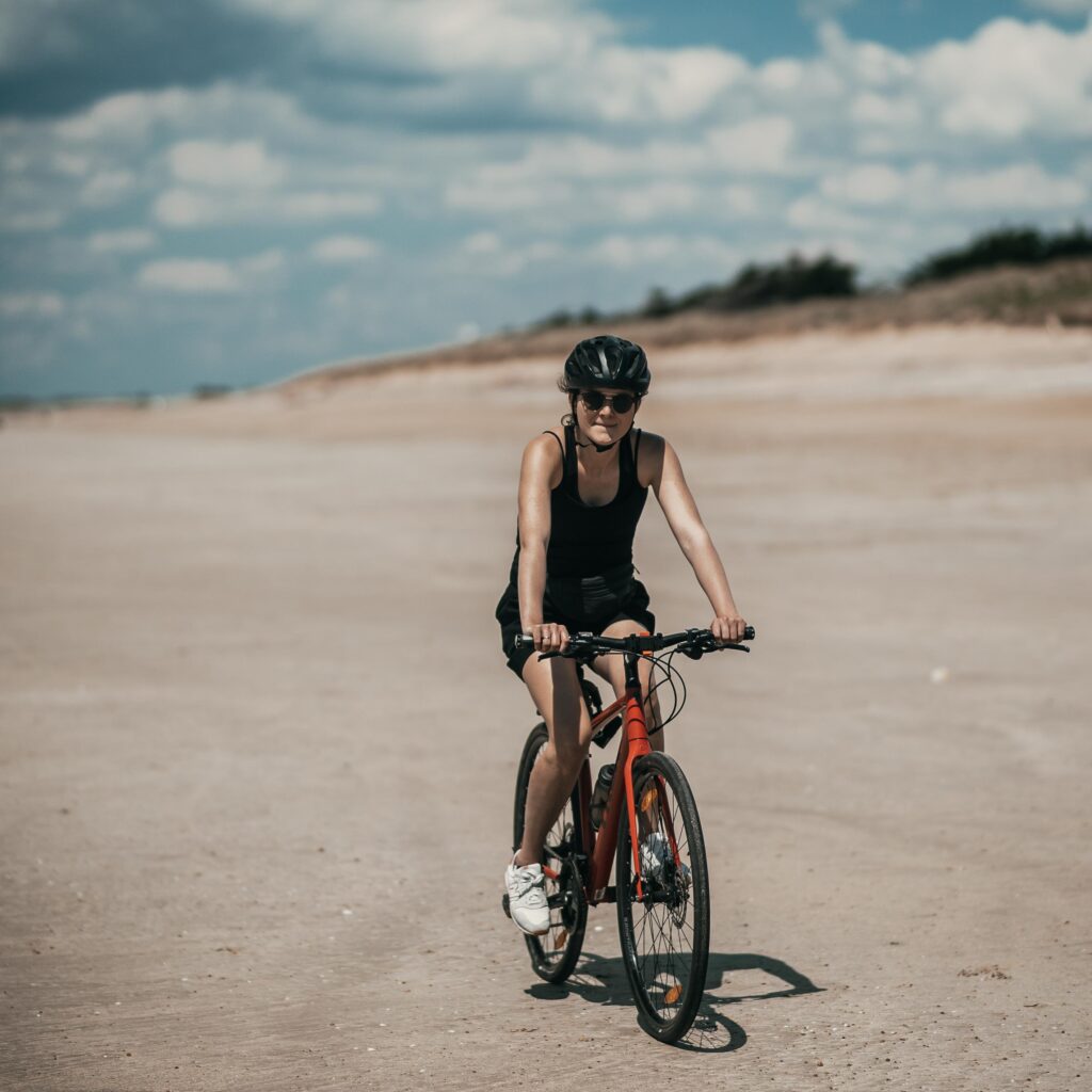 Rowerzystka w kasku jadąca rowerem po plaży
