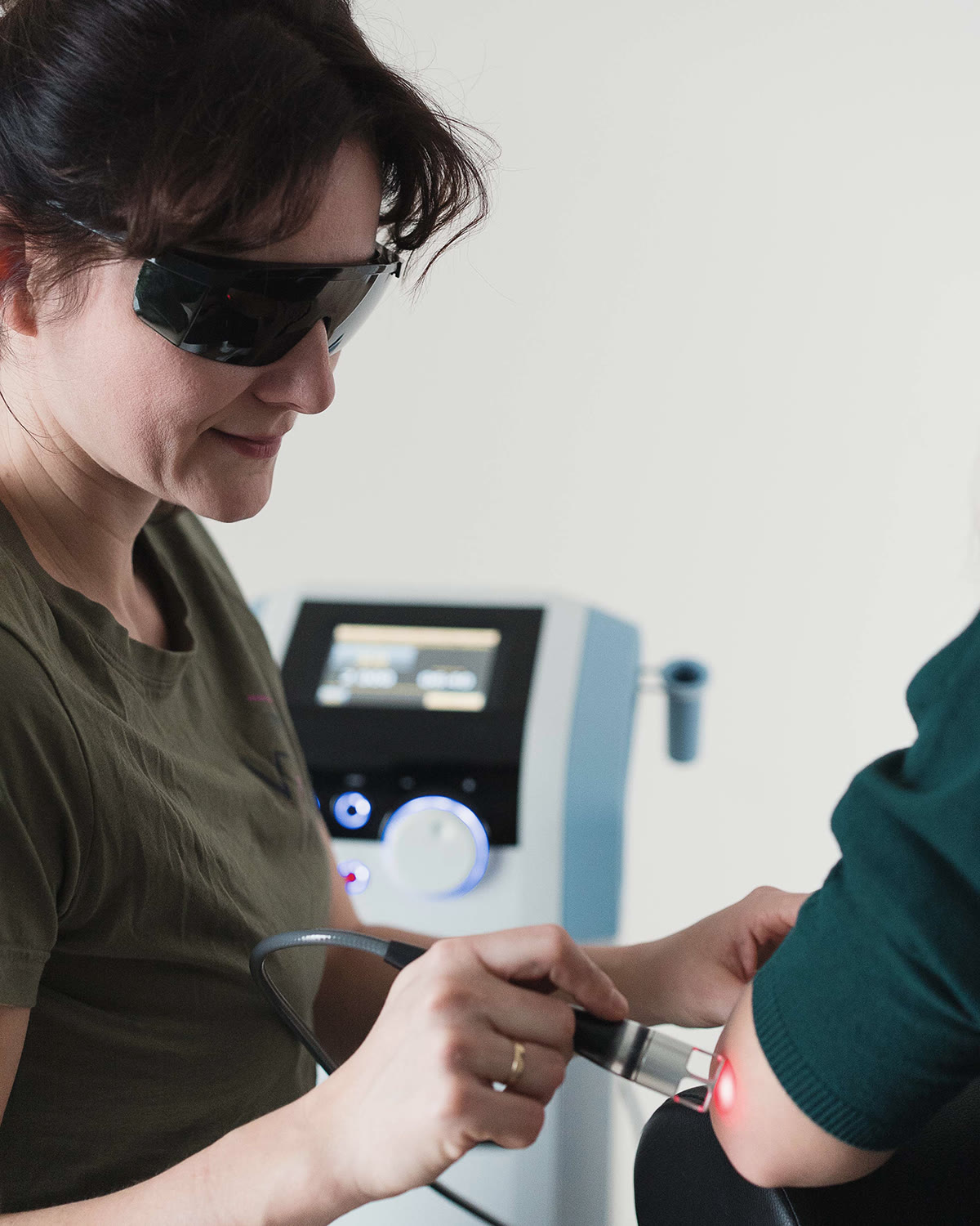 Fizjoterapeutka w okularach ochronnych wykonuje laseroterapię okolicy łokcia