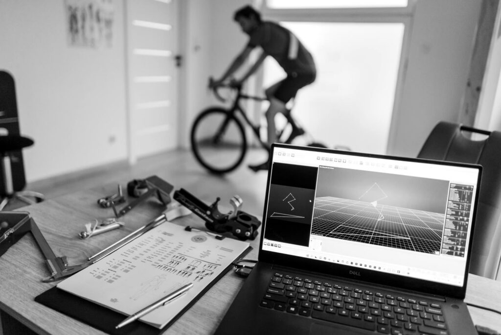 Stanowisko bike fittingu — rowerzysta na trenażerze i analiza 3D na laptopie